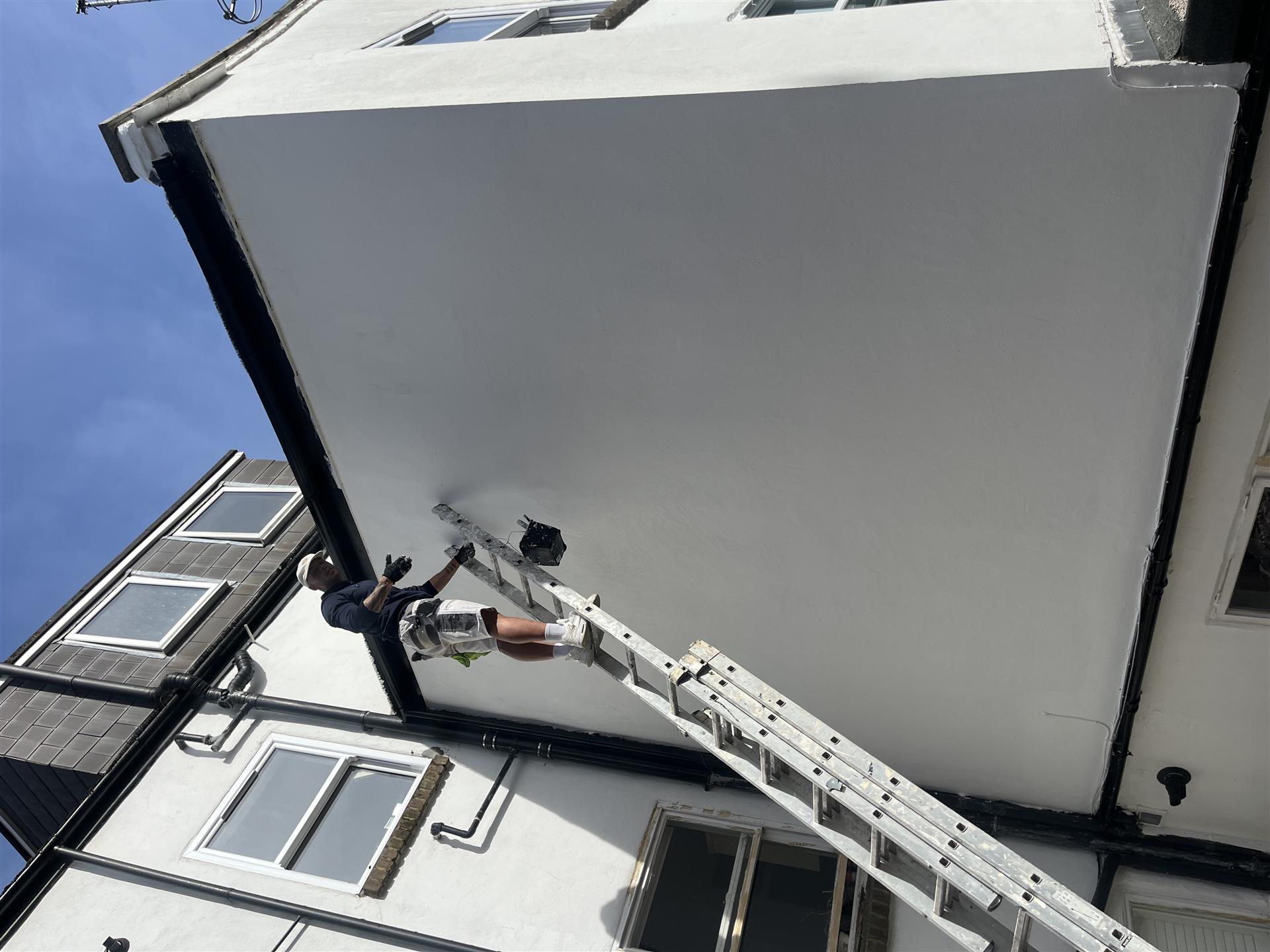 Painter on ladder painting gable end of house, Essex